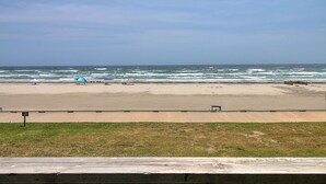Una playa con una cerca de madera al frente, una orilla arenosa y el océano de fondo.