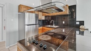 A modern kitchen with a stainless steel refrigerator, a gas stove, and wooden cabinets. - Gulfstream Condos Unit 215 | Beachfront Balcony | Pool & Hot Tub (Corpus Christi)