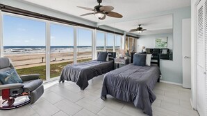 A bedroom with two beds, a chair, a ceiling fan, and a view of the beach. - Gulfstream Condos Unit 215 | Beachfront Balcony | Pool & Hot Tub (Corpus Christi)