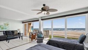 A room with a large window overlooking the beach, a ceiling fan, and a sofa. - Gulfstream Condos Unit 215 | Beachfront Balcony | Pool & Hot Tub (Corpus Christi)