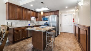 A kitchen with wooden cabinets, a central island with stools, stainless steel appliances, and a tiled floor. - Gulfstream Condos Unit 216 | Direct Gulf Views | Pool, Hot Tub (Corpus Christi)