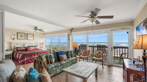 A spacious living room with a large window overlooking the ocean, a ceiling fan, and a cozy seating area with a sofa and chairs. - Gulfstream Condos Unit 216 | Direct Gulf Views | Pool, Hot Tub (Corpus Christi)