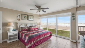 A bedroom with a large bed, a ceiling fan, and a view of the beach through large windows. - Gulfstream Condos Unit 216 | Direct Gulf Views | Pool, Hot Tub (Corpus Christi)