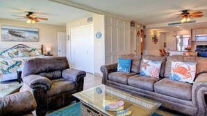 A living room with two brown leather sofas, a glass coffee table, and a ceiling fan. - Gulfstream Condos Unit 217 | Gulf-Front View with Beach Balcony & Pool (Corpus Christi)