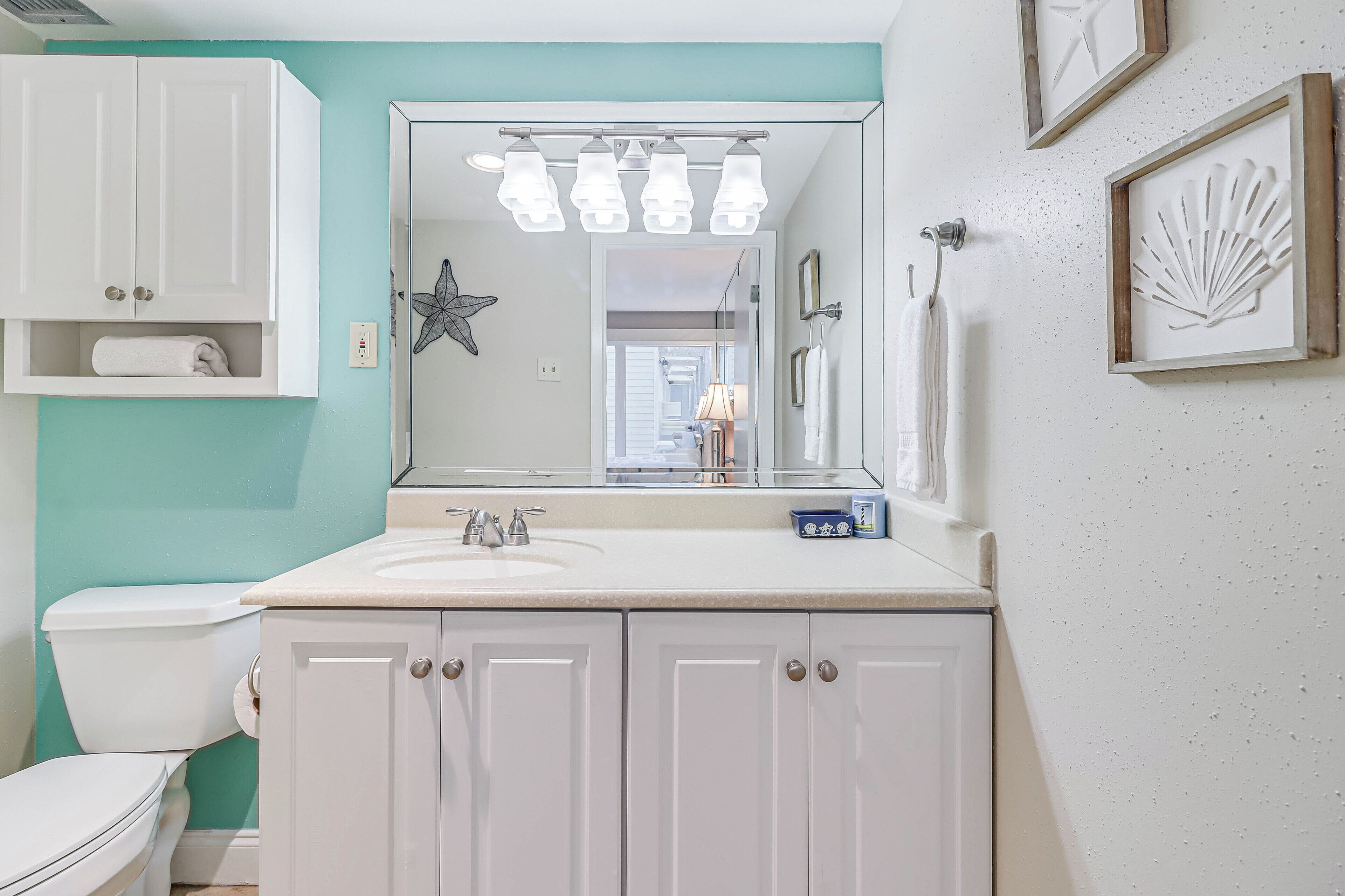 A bathroom with a white sink, a toilet, and a mirror above the sink. There are framed pictures on the wall and a star decoration.