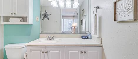 A bathroom with a white sink, a toilet, and a mirror above the sink. There are framed pictures on the wall and a star decoration.