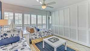 Una habitación con cama, sofá, ventilador de techo y ventana con persianas.