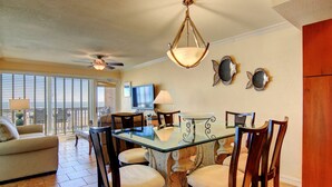 A dining area with a glass table, wooden chairs, and a ceiling fan. - Gulfstream Condos Unit 312 | Balcony with Beach Front Views, Pool & Hot Tub (Corpus Christi)