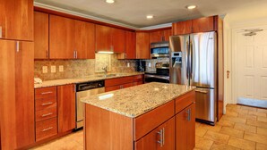 A kitchen with wooden cabinets, granite countertops, stainless steel appliances, and a tiled backsplash. - Gulfstream Condos Unit 312 | Balcony with Beach Front Views, Pool & Hot Tub (Corpus Christi)