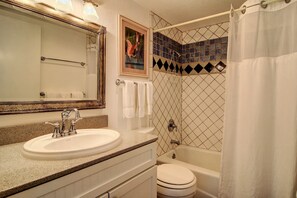 Features a spacious bathroom with a large mirror, sink, and toilet, plus a shower area with a glass door and shower curtain.