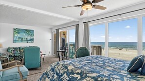 Ein Hotelzimmer mit einem großen Bett, einem Deckenventilator, Blick auf den Strand, einem Sessel und einem Tisch.