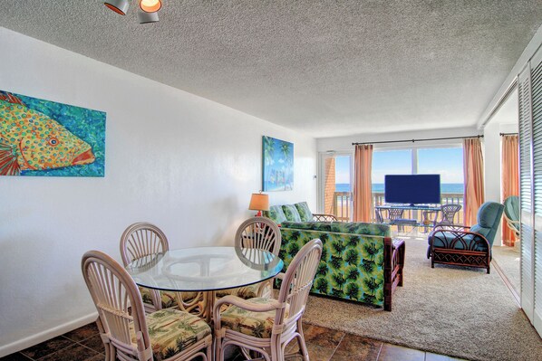 Relax in this spacious living area with a dining table, sofa, and TV, offering a view of the outdoors through large windows.