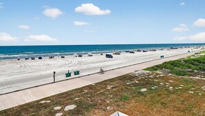 Ein Strand mit gepflastertem Gehweg, parkenden Autos und blauem Himmel.