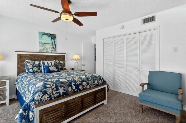 Une chambre à coucher avec un lit, une chaise, un ventilateur de plafond, un tableau et un placard.
