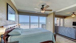 Hotelkamer met een groot bed, een plafondventilator, uitzicht op het strand en een balkon met een televisie.