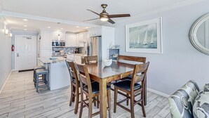 Une cuisine moderne avec des meubles blancs, un îlot central et un coin repas doté de chaises en bois.