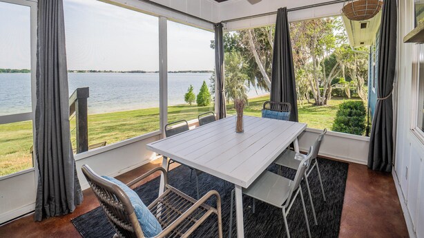 Ein Zimmer mit großem Fenster mit Blick auf ein Gewässer, einem weißen Tisch und Korbstühlen.