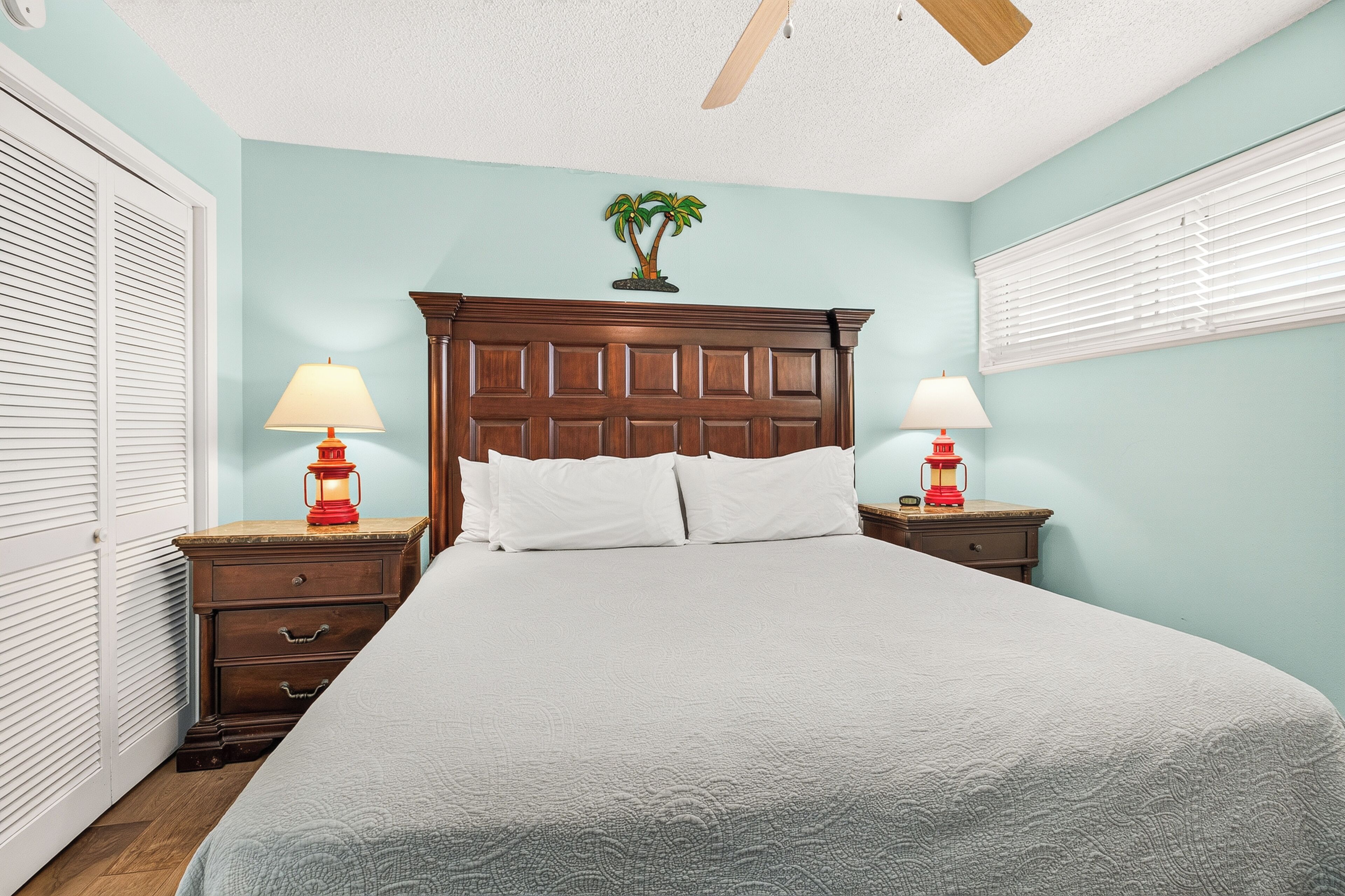 A bedroom with a bed, two nightstands with lamps, a wooden headboard, and a ceiling fan.