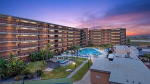 A multi-story hotel with a swimming pool, outdoor seating, and palm trees. - Gulfstream Condo Unit #401 Heated Pool & Hot Tub | Pickleball Court (Corpus Christi)