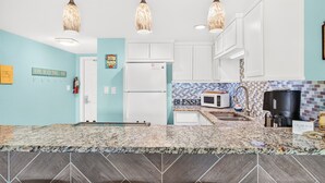 A kitchen with white cabinets, a granite countertop, a refrigerator, a microwave, a coffee maker, and a hanging towel rack. - Gulfstream Condo Unit #401 Heated Pool & Hot Tub | Pickleball Court (Corpus Christi)