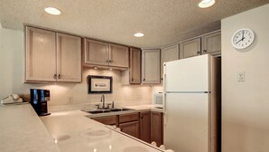 A kitchen with wooden cabinets, a white refrigerator, a double sink, and a clock on the wall. - Gulfstream Condos Unit 402 | Private Balcony | Pool, Hot Tub & BBQ (Corpus Christi)