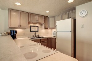 A kitchen with wooden cabinets, a white refrigerator, a double sink, and a clock on the wall. - Gulfstream Condos Unit 402 | Private Balcony | Pool, Hot Tub & BBQ (Corpus Christi)
