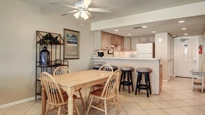 A kitchen with a wooden dining table, four chairs, a ceiling fan, and a kitchen island with stools. - Gulfstream Condos Unit 402 | Private Balcony | Pool, Hot Tub & BBQ (Corpus Christi)