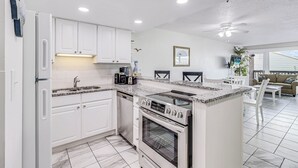 A modern kitchen with white cabinets, a granite countertop, a built-in oven, and a dining area with a white table and chairs. - Unit 403 Private Balcony/Heated Pool & Hot Tub / BBQ (Corpus Christi)