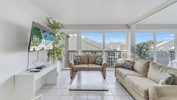 A spacious living room with a beige sofa, a coffee table, and a TV mounted on the wall. - Unit 403 Private Balcony/Heated Pool & Hot Tub / BBQ (Corpus Christi)