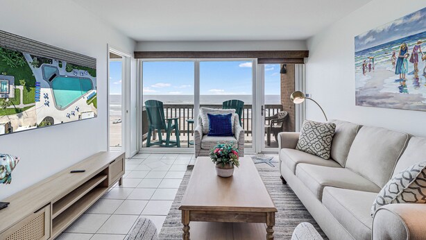 Un salon spacieux avec une grande télévision, une table basse et un canapé. Il y a un balcon avec vue sur la plage.