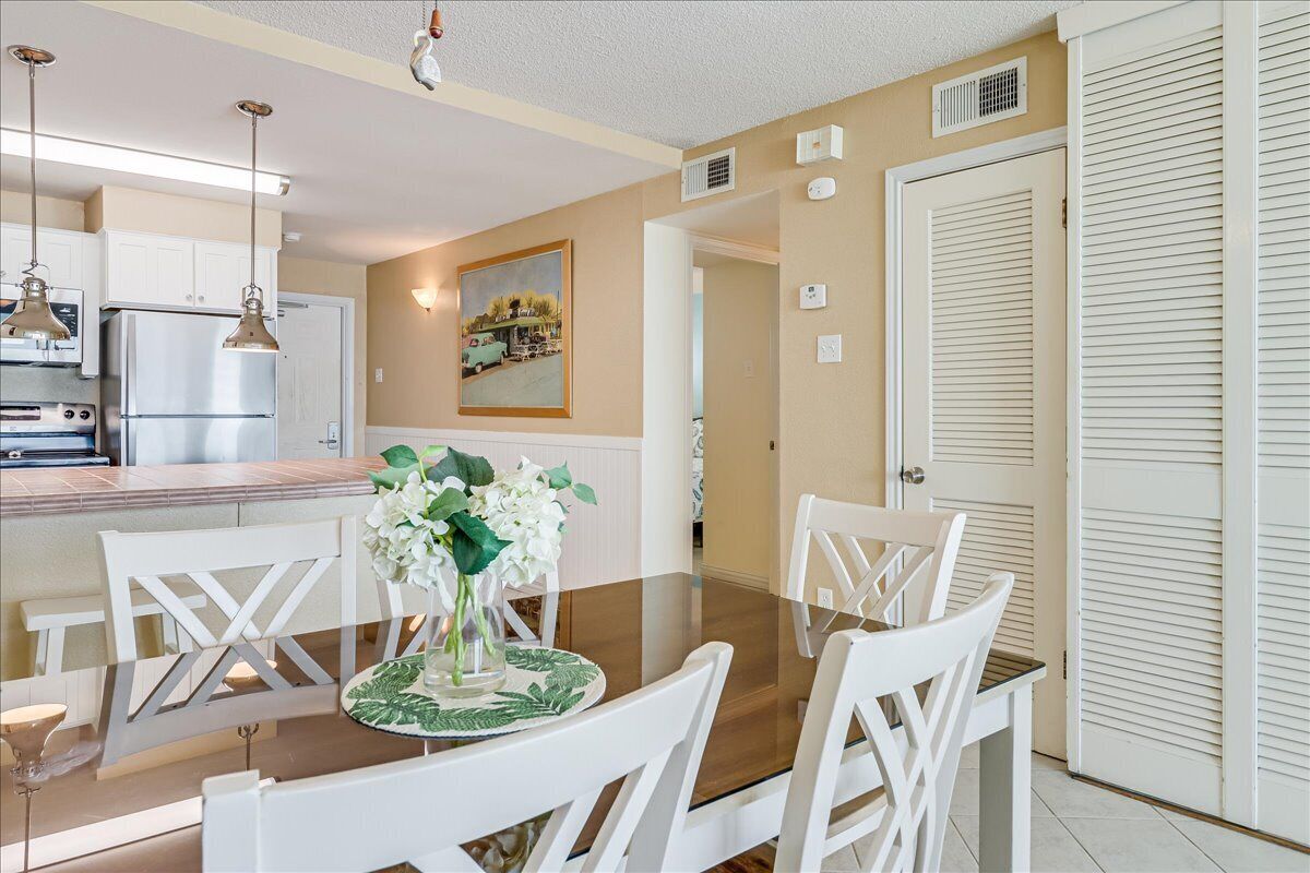 A dining area with a glass-top table, white chairs, and a vase of flowers.