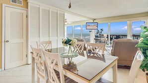 A dining area with a table and chairs, a ceiling fan, and a view of the ocean through large windows. - Gulfstream Condos Unit 412 | Gulf- Front View (Corpus Christi)