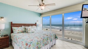 A bedroom with a large bed, a ceiling fan, a TV, and a view of the beach. - Gulfstream Condos Unit 412 | Gulf- Front View (Corpus Christi)