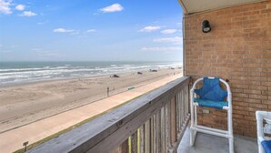 A balcony with a view of a beach, a brick wall, and a blue chair. - Gulfstream Condos Unit 412 | Gulf- Front View (Corpus Christi)