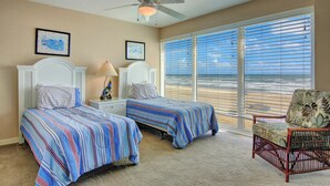 A bedroom with two beds, a ceiling fan, a chair, and a large window with blinds.