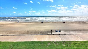 A beach with a clear sky, waves, and a few cars parked on the sand.