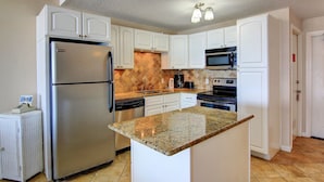 A kitchen with white cabinets, a stainless steel refrigerator, a granite countertop, and a microwave.