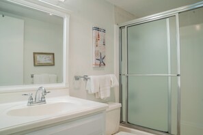 A bathroom with a white sink, a large mirror, and a glass-enclosed shower. - Gulfstream Condos Unit 417 | Pool & Hot Tub | Balcony with Gulf Front Views! (Corpus Christi)
