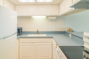 A kitchen with white cabinets, a sink, a stove, and a microwave. - Gulfstream Condos Unit 417 | Pool & Hot Tub | Balcony with Gulf Front Views! (Corpus Christi)