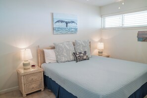 A bedroom with a bed, two bedside tables with lamps, a wall clock, and a painting. - Gulfstream Condos Unit 417 | Pool & Hot Tub | Balcony with Gulf Front Views! (Corpus Christi)