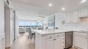A modern kitchen with white cabinetry, a central island, and a view to the outdoors. - Gulfstream Corner Unit 418 | Wraparound Beachfront Balcony | Pool, Hot Tub (Corpus Christi)