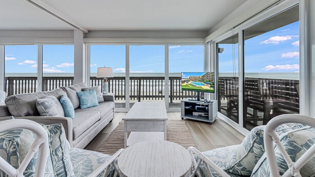 A balcony with a view of the ocean, furnished with a sofa, chairs, and a coffee table. - Gulfstream Corner Unit 418 | Wraparound Beachfront Balcony | Pool, Hot Tub (Corpus Christi)