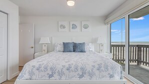 A bedroom with a large bed, a nightstand, a lamp, and a view of the beach through a sliding door. - Gulfstream Corner Unit 418 | Wraparound Beachfront Balcony | Pool, Hot Tub (Corpus Christi)