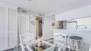 Une cuisine moderne avec des meubles blancs, une table à manger en verre et des chaises blanches, ainsi qu’un tabouret de bar.