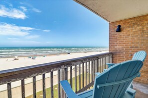 A balcony with a view of the beach, a brick wall, and two blue chairs. - Gulfstream Condos Unit 508 | Gulf Views & Beachfront Balcony | Pool, Hot Tub (Corpus Christi)