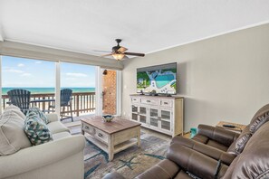 A living room with a view of the ocean, a ceiling fan, and a television mounted on the wall. - Gulfstream Condos Unit 508 | Gulf Views & Beachfront Balcony | Pool, Hot Tub (Corpus Christi)