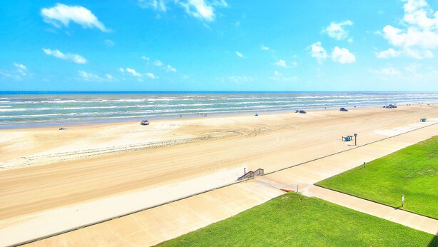 A beach view with a clear sky, sandy beach, and a grassy area. - Gulfstream Condos Unit 508 | Gulf Views & Beachfront Balcony | Pool, Hot Tub (Corpus Christi)