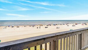 A beach view from a balcony with a wooden railing, sandy beach, and ocean in the background. - Gulfstream Condos Unit 511 | Gulf-Front Balcony | Pool & Hot Tub (Corpus Christi)