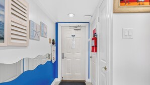 A hallway with a white door, a blue accent wall, a black doormat, and a fire extinguisher mounted on the wall. - Gulfstream Condos Unit 511 | Gulf-Front Balcony | Pool & Hot Tub (Corpus Christi)