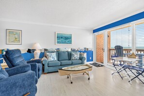 A living room with a blue sofa, armchairs, a coffee table, and a view of the sea through large windows.